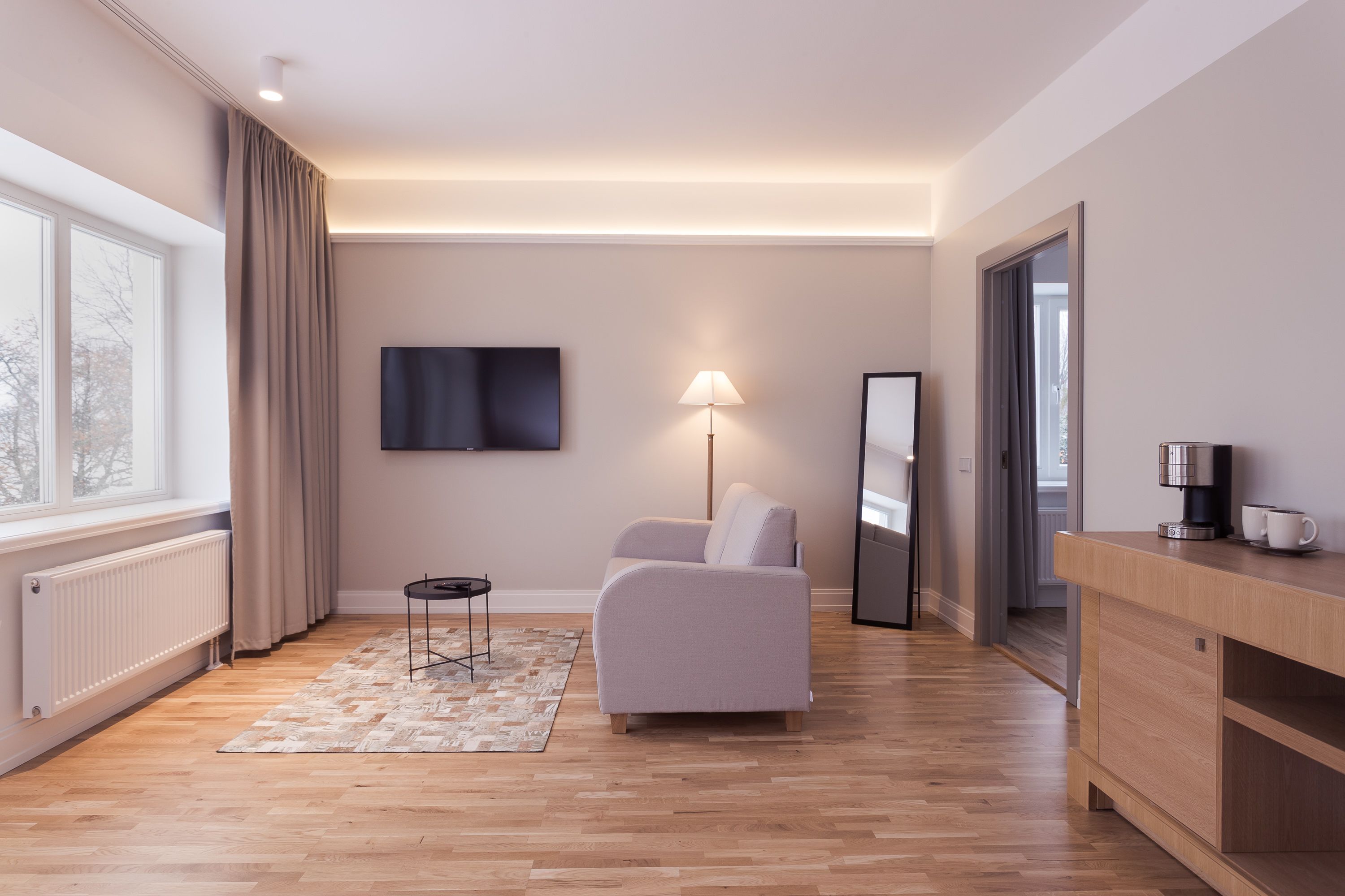 A modern living room with a sofa, a coffee machine, and a TV on the wall.