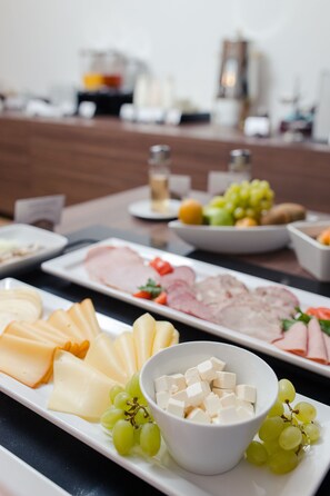 A table with various cheeses, meats, and fruits.
