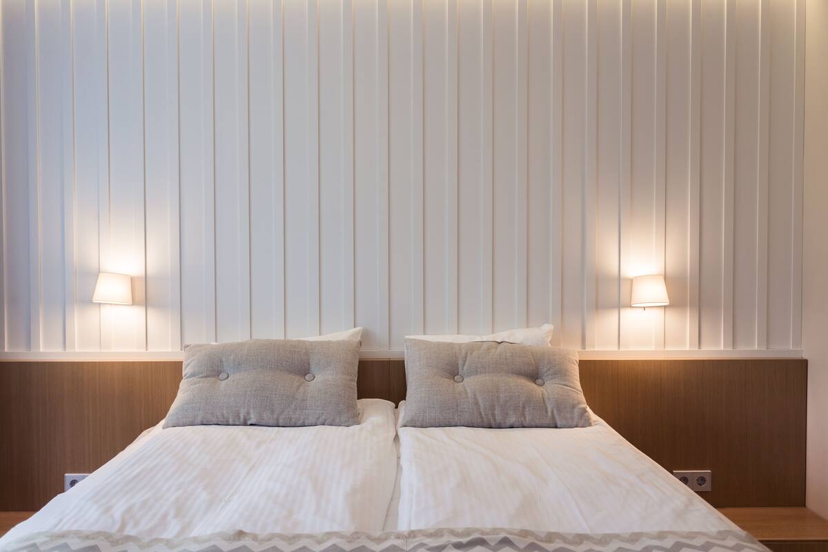 A double bed with two bedside lamps, a wooden headboard, and a chevron-patterned bed skirt.