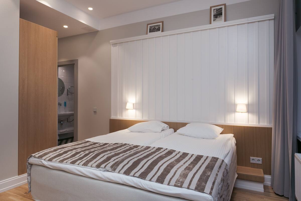 A bedroom with a bed, bedside lamps, a wooden wardrobe, and a shower area.
