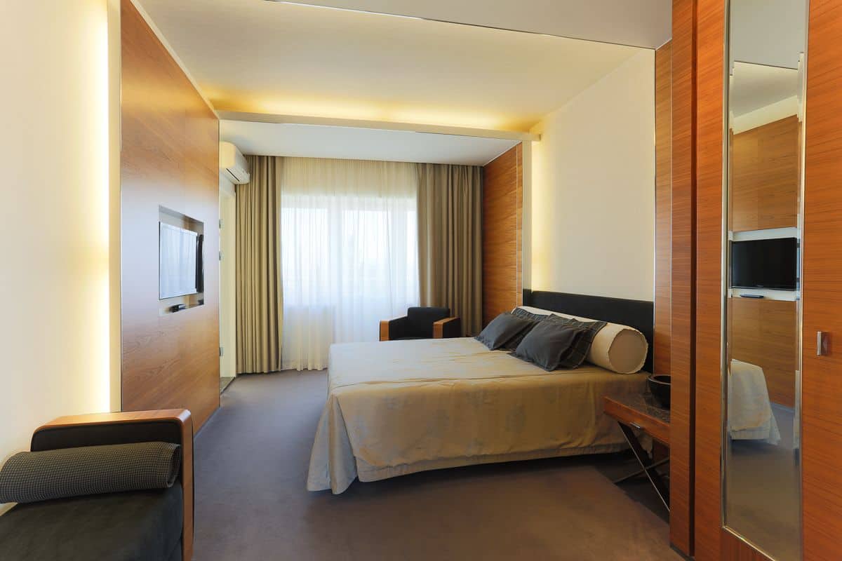 A modern hotel room with a large bed, a desk, a chair, and a TV.