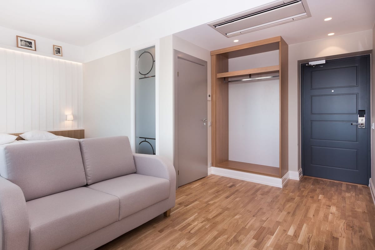 A modern hotel room with a bed, a sofa, a wardrobe, and a door.