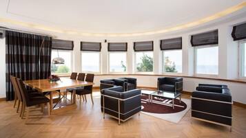 Ein modernes Wohnzimmer mit einem Holzesstisch, schwarzen Sofas und großen Fenstern mit Vorhängen.