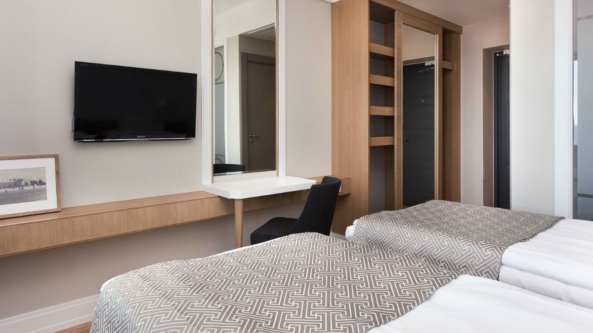 A hotel room with a bed, a desk, a chair, a television, and a wardrobe.