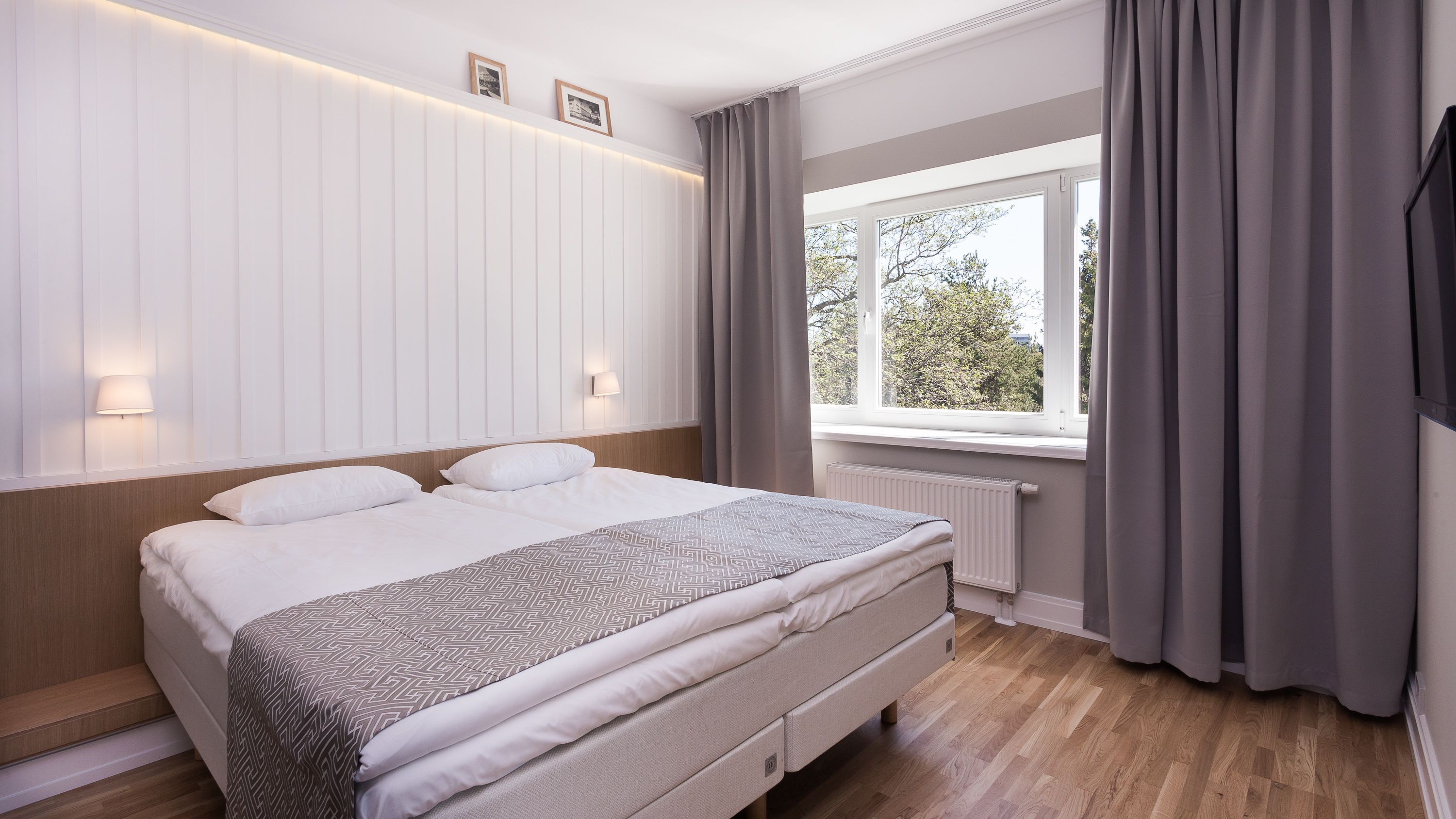 Une chambre moderne avec un grand lit, une fenêtre avec des rideaux et un luminaire fixé au mur.