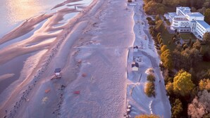 An aerial view of a coastal area with a beach, a large white building with multiple floors, and surrounding trees. - Rannahotell (Parnu)
