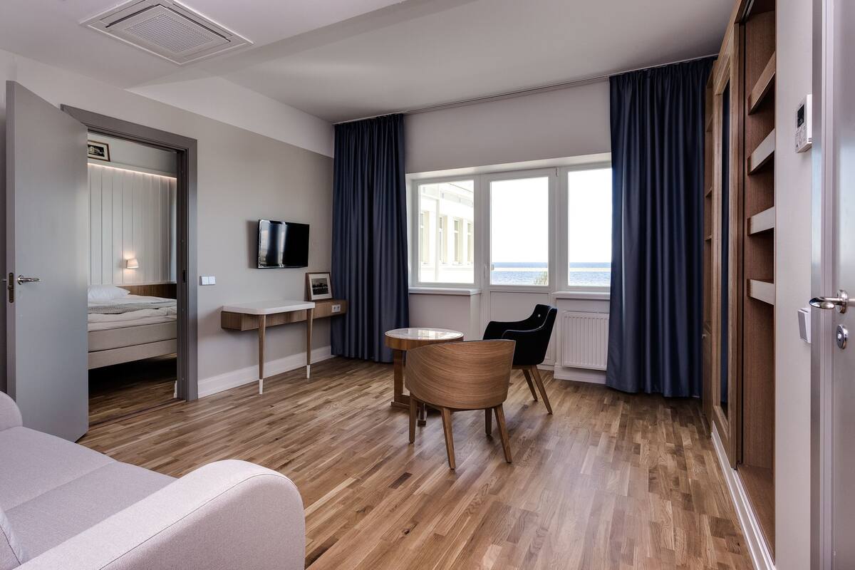 A modern hotel room with a bed, a desk, a chair, and a view of the sea.