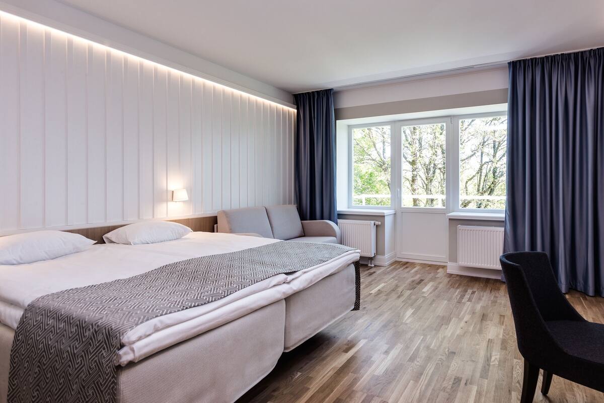 A modern hotel room with a large bed, a desk, and a window with curtains.