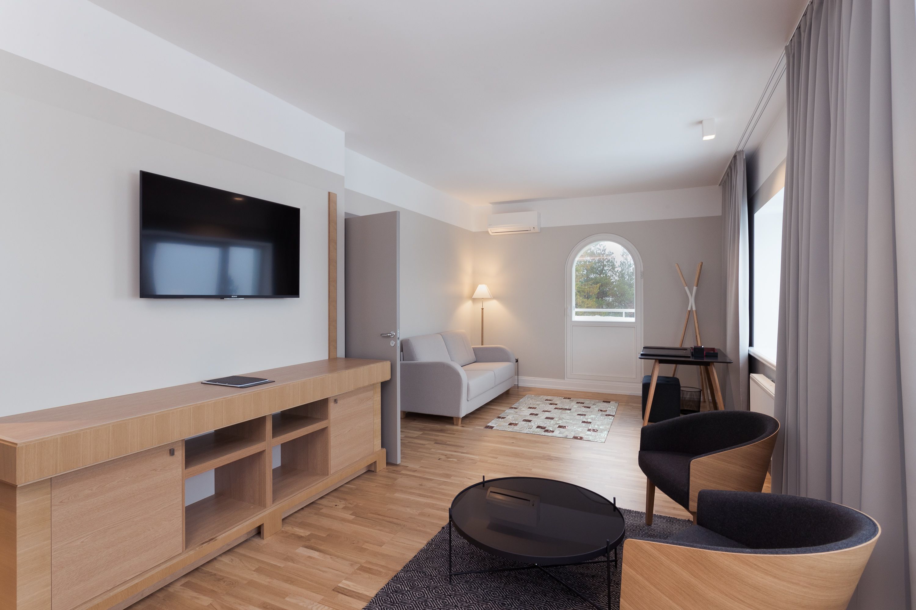 A modern living room with a flat-screen TV, wooden furniture, a sofa, and a dining area.