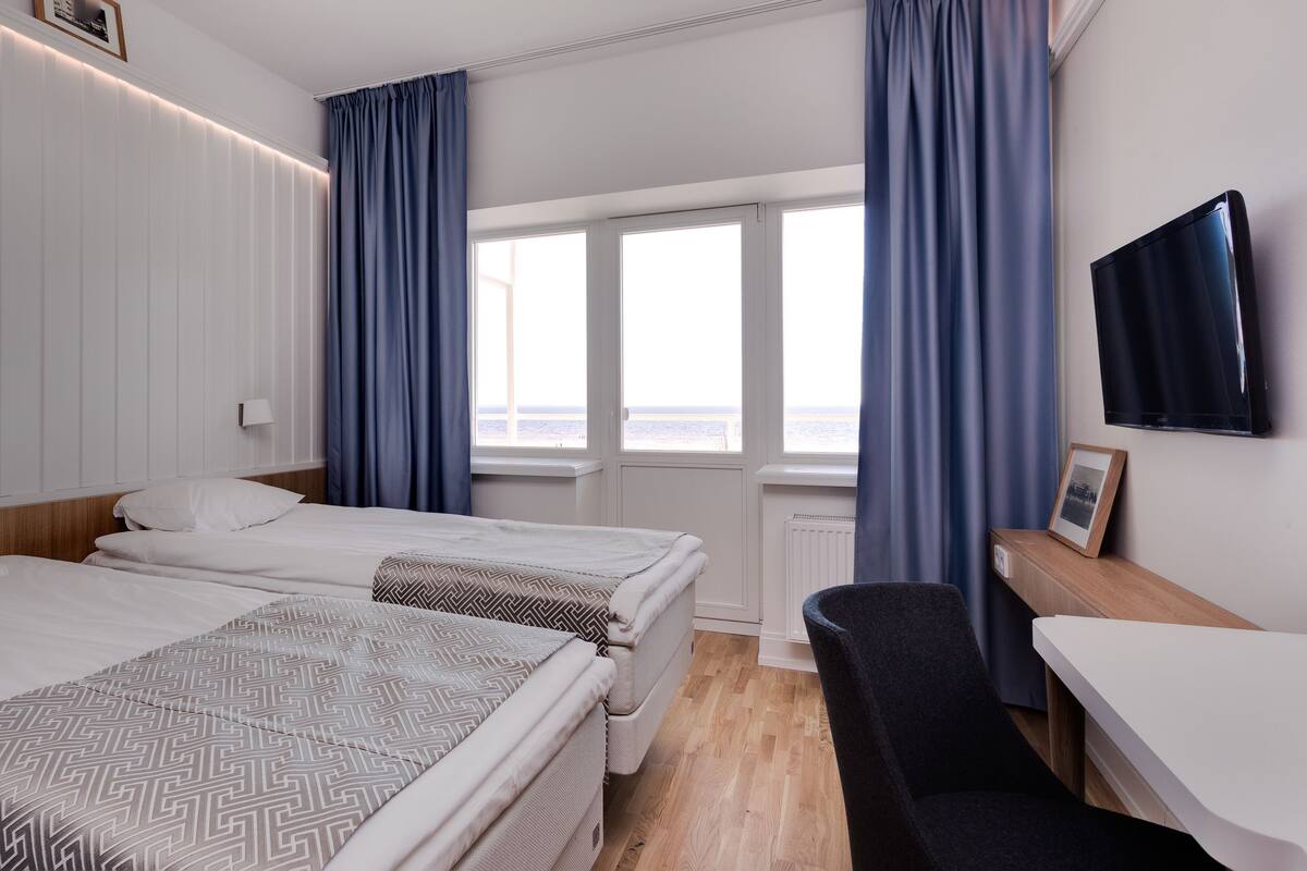 A hotel room with two beds, a desk, a chair, a TV, and a window with curtains.