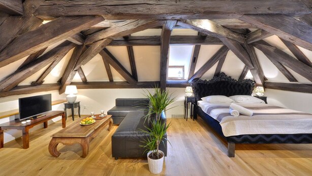 Un dormitorio tipo loft con vigas de madera a la vista, una cama, un sofá, un televisor y una mesa de comedor con fruta.