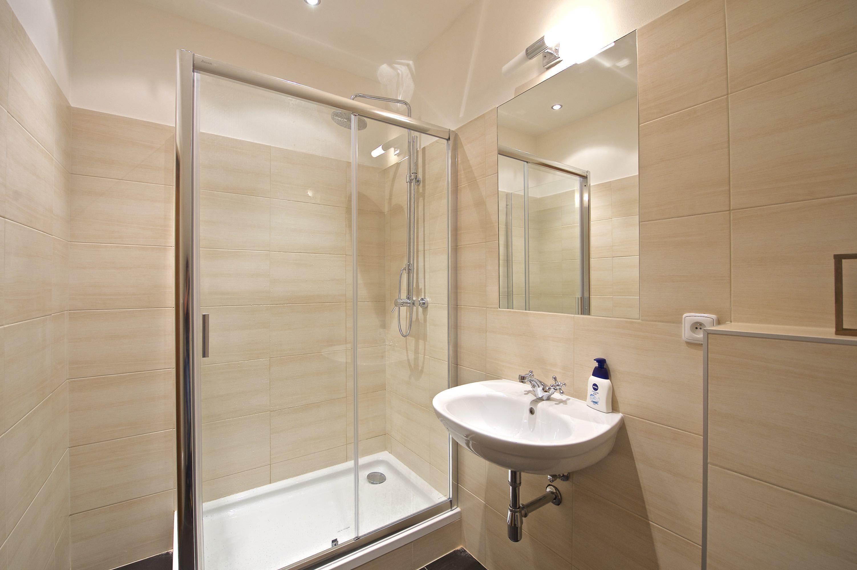 Een moderne badkamer met een douche in een glazen cabine, een wastafel met spiegel en beige betegelde wanden.