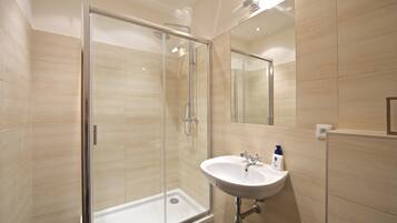 Een moderne badkamer met een douche in een glazen cabine, een wastafel met spiegel en beige betegelde wanden.