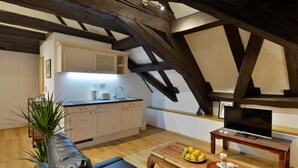 Una sala de estar acogedora con un sofá, una mesa de centro con frutas, un televisor sobre un mueble bajo y una zona de cocina con armarios y un fregadero.