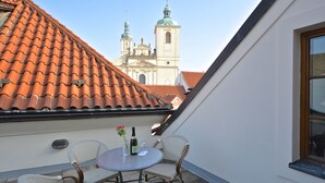 Una terraza con techo de tejas, una mesa con sillas y vista a una iglesia con dos cúpulas.