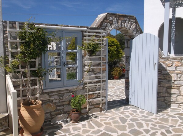 A stone-walled courtyard with a white gate, potted plants, and a tiled floor.