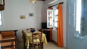 A dining area with a table set for two, a television on a stand, and a window with curtains.