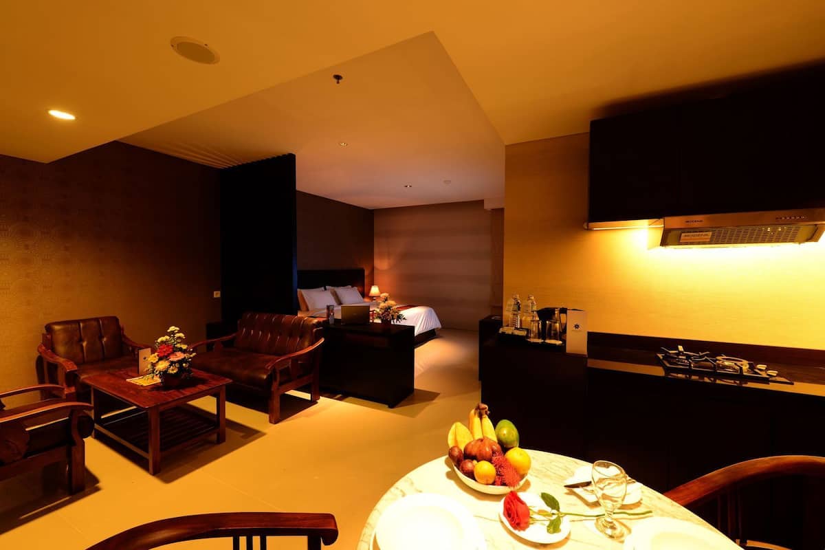 A hotel room with a dining area, a bed, a desk with a laptop, and a minibar.