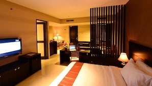 Een hotelkamer met een bed, een bureau met een laptop, een televisie en een zithoek met stoelen.