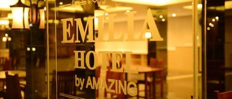 Una ventana de vidrio con el texto "EMILIA HOTEL by AMAZING" en una tipografía estilizada.