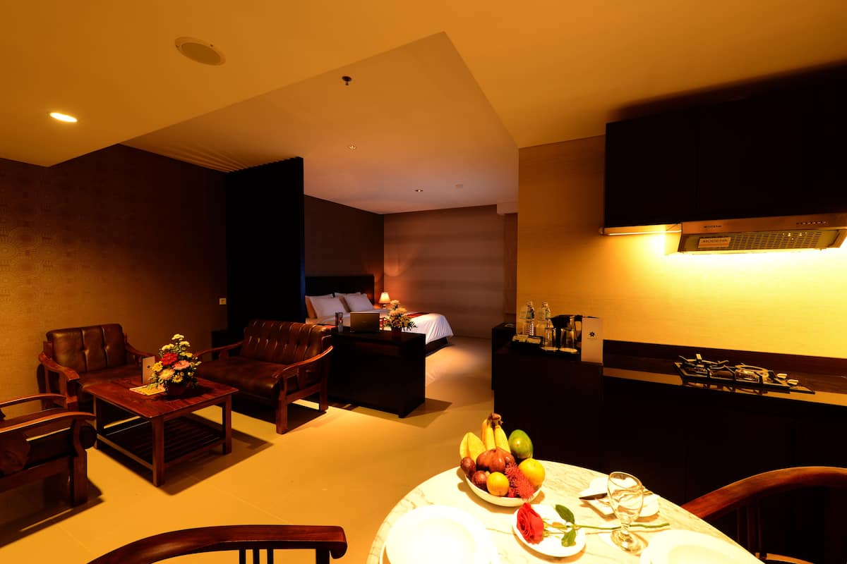 A hotel room with a dining area, a sofa set, a flat-screen TV, and a kitchenette.
