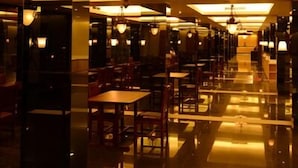 Een hotel lobby met een kroonluchter in het midden, een spiegelende vloer en rijen tafels en stoelen.