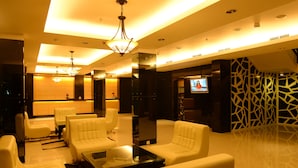 Een moderne lobby met witte leren banken, een glazen salontafel en een televisiescherm.