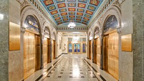 Un vaste hall d’entrée avec un sol en marbre, un plafond richement décoré et des ascenseurs.