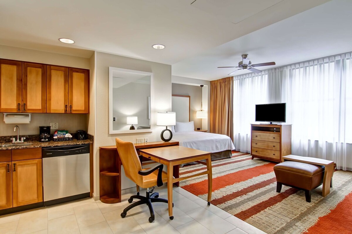 Habitación de hotel con cama, escritorio, silla, televisión y kitchenette.