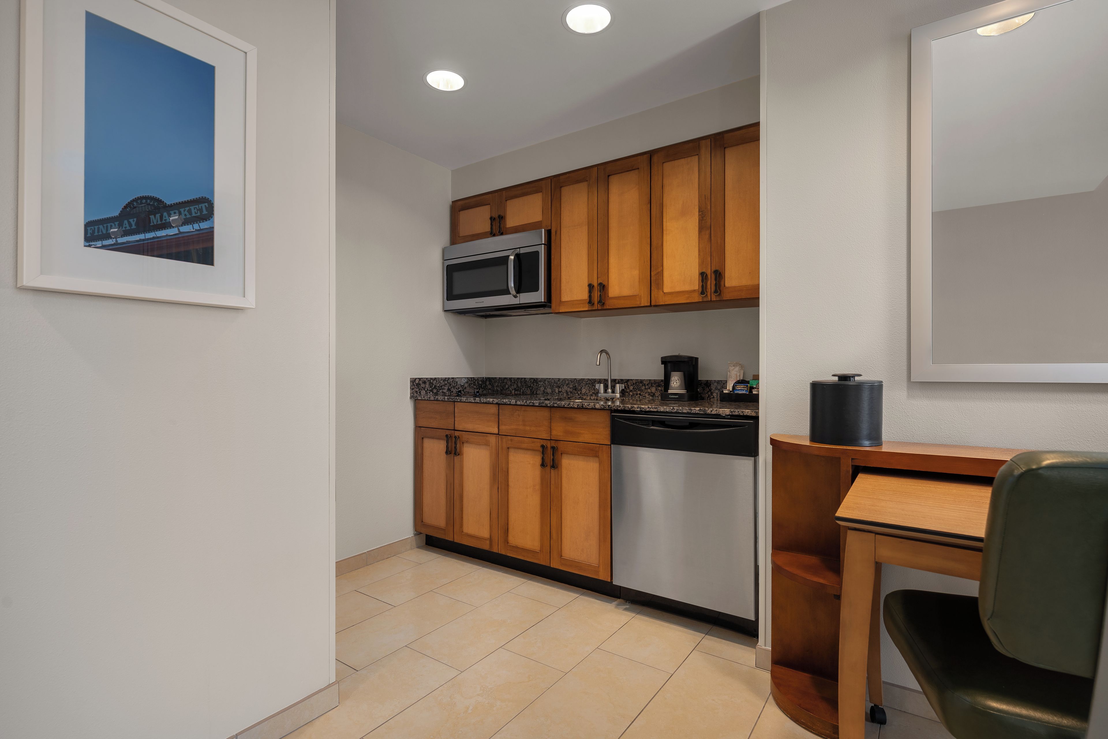 A compact kitchen with wooden cabinets, a stainless steel microwave, a dishwasher, and a countertop with a coffee maker.