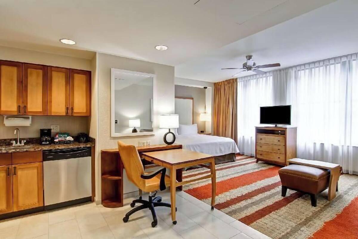 Een hotelkamer met een bed, bureau, stoel, televisie en een kitchenette.