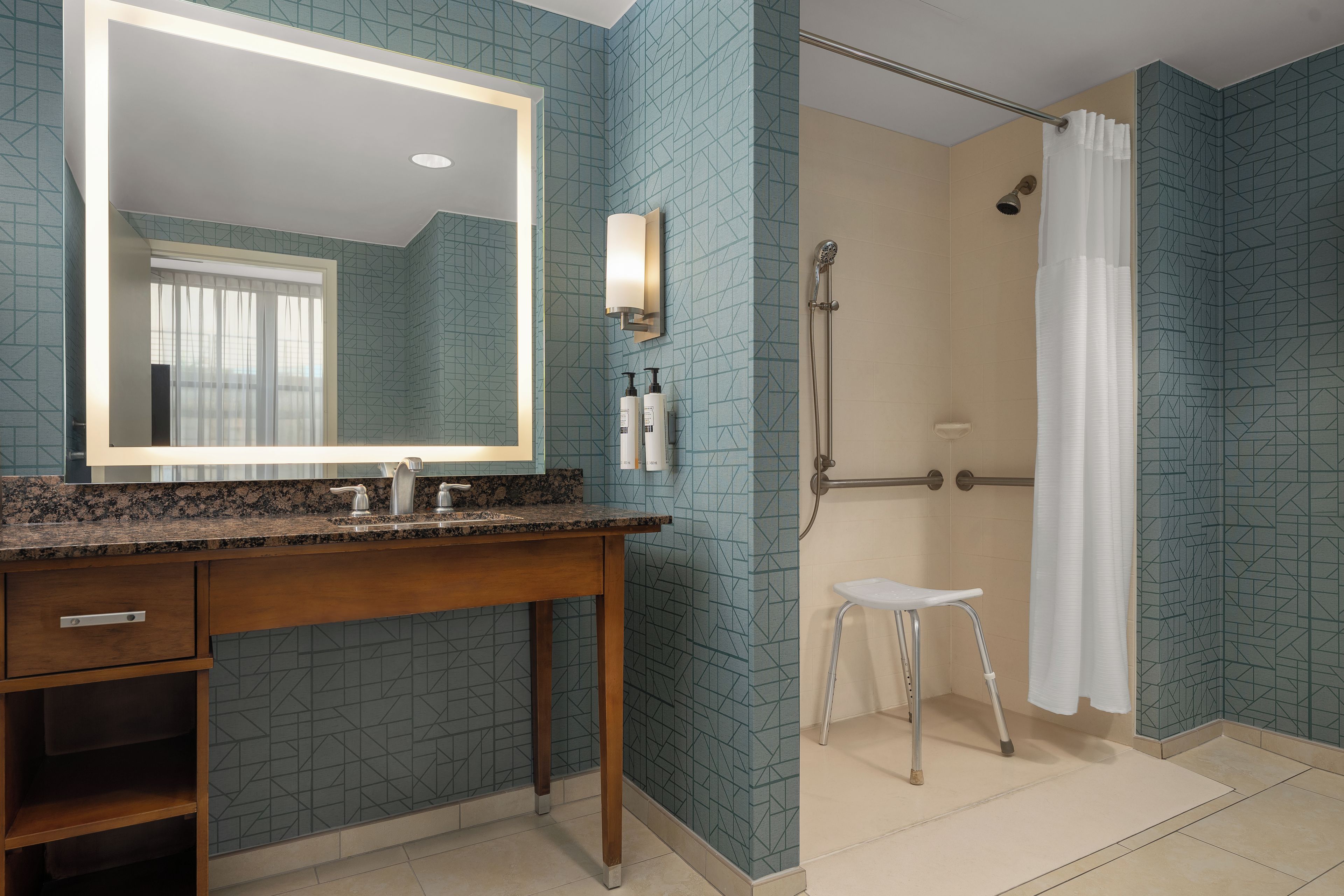 A bathroom with a granite countertop, a wooden vanity, a large mirror, a shower with a handheld showerhead, and a white shower curtain.