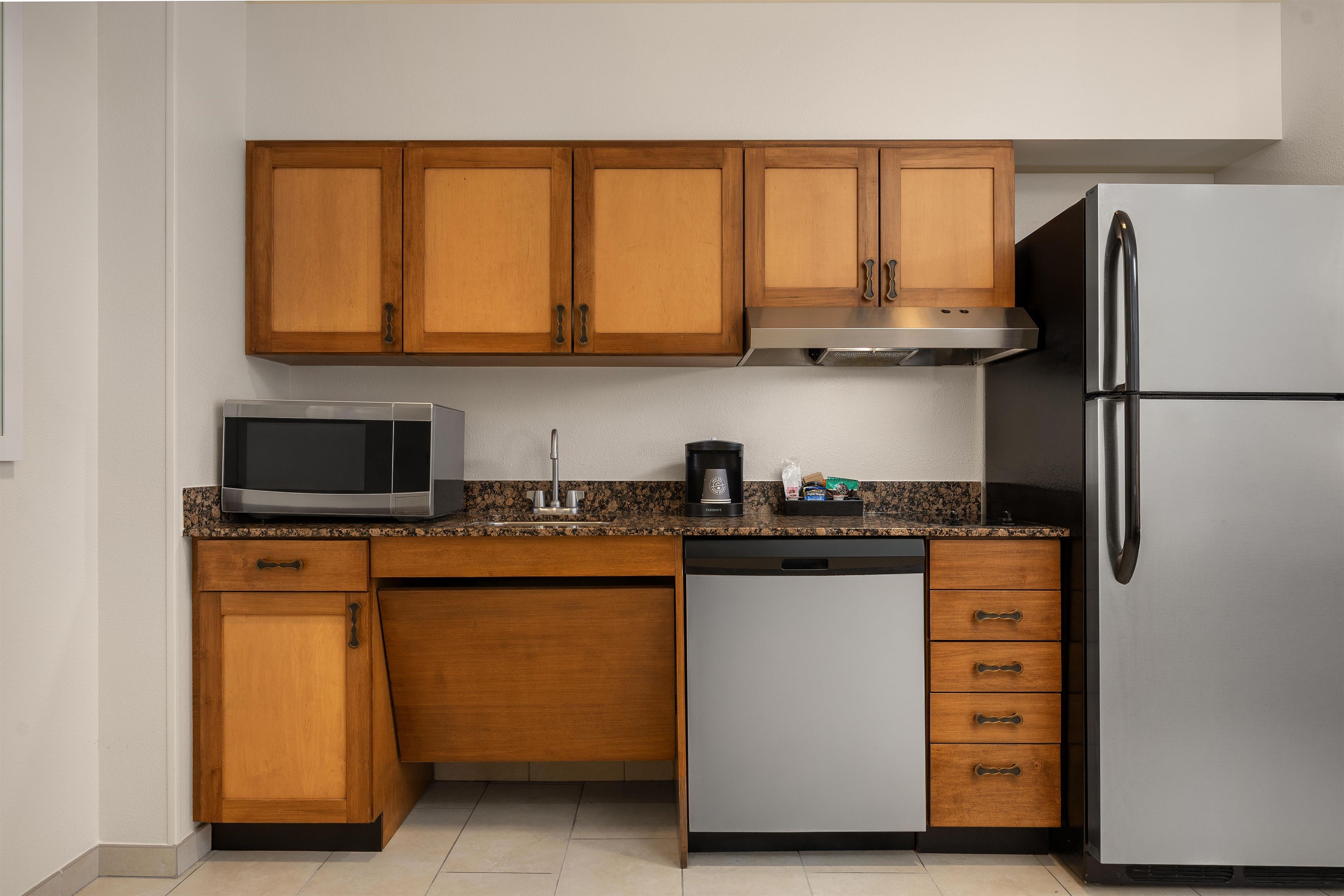 A compact kitchen with wooden cabinets, a microwave, a coffee maker, and a refrigerator.