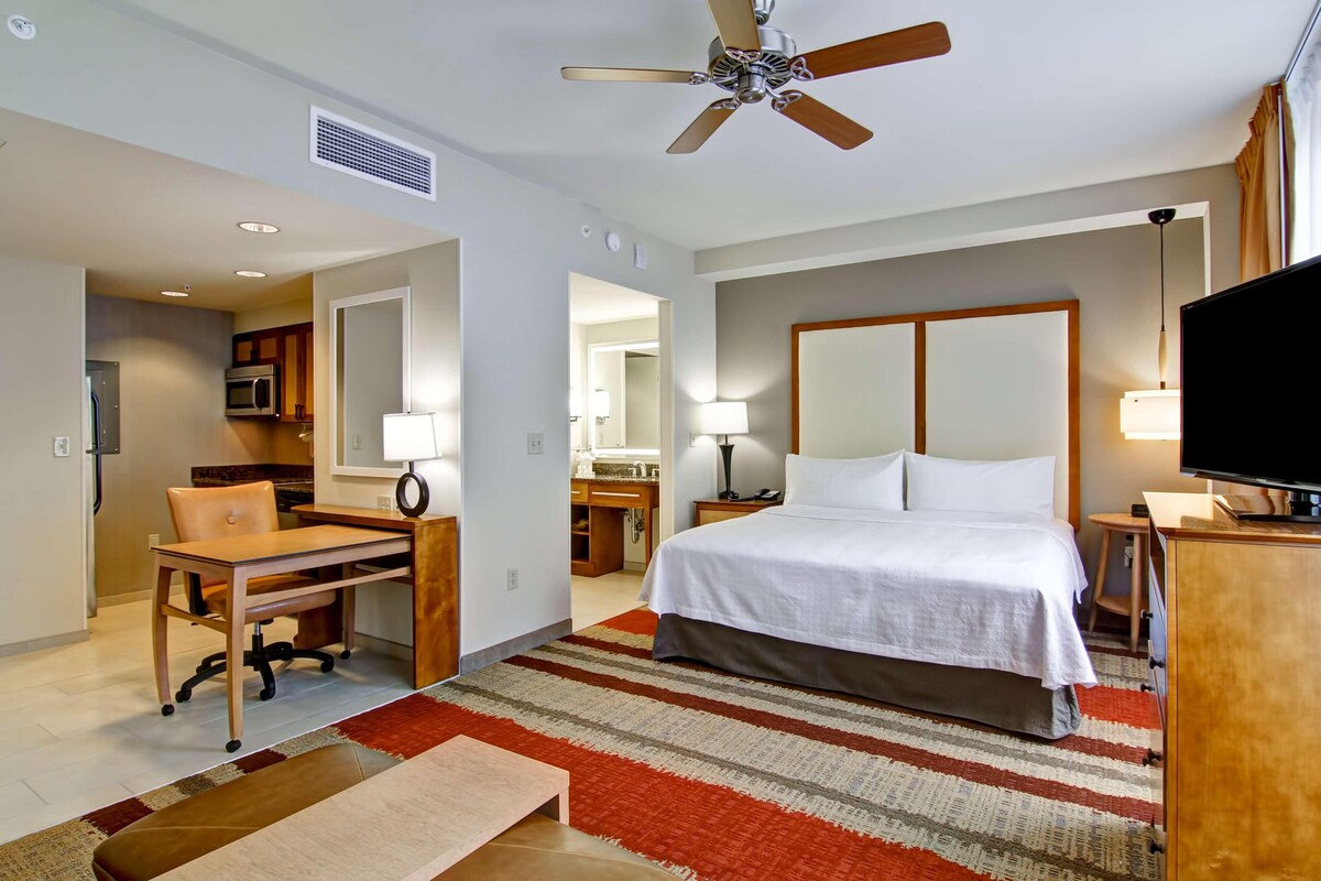 Habitación de hotel con cama, escritorio, silla, televisor y ventilador de techo.
