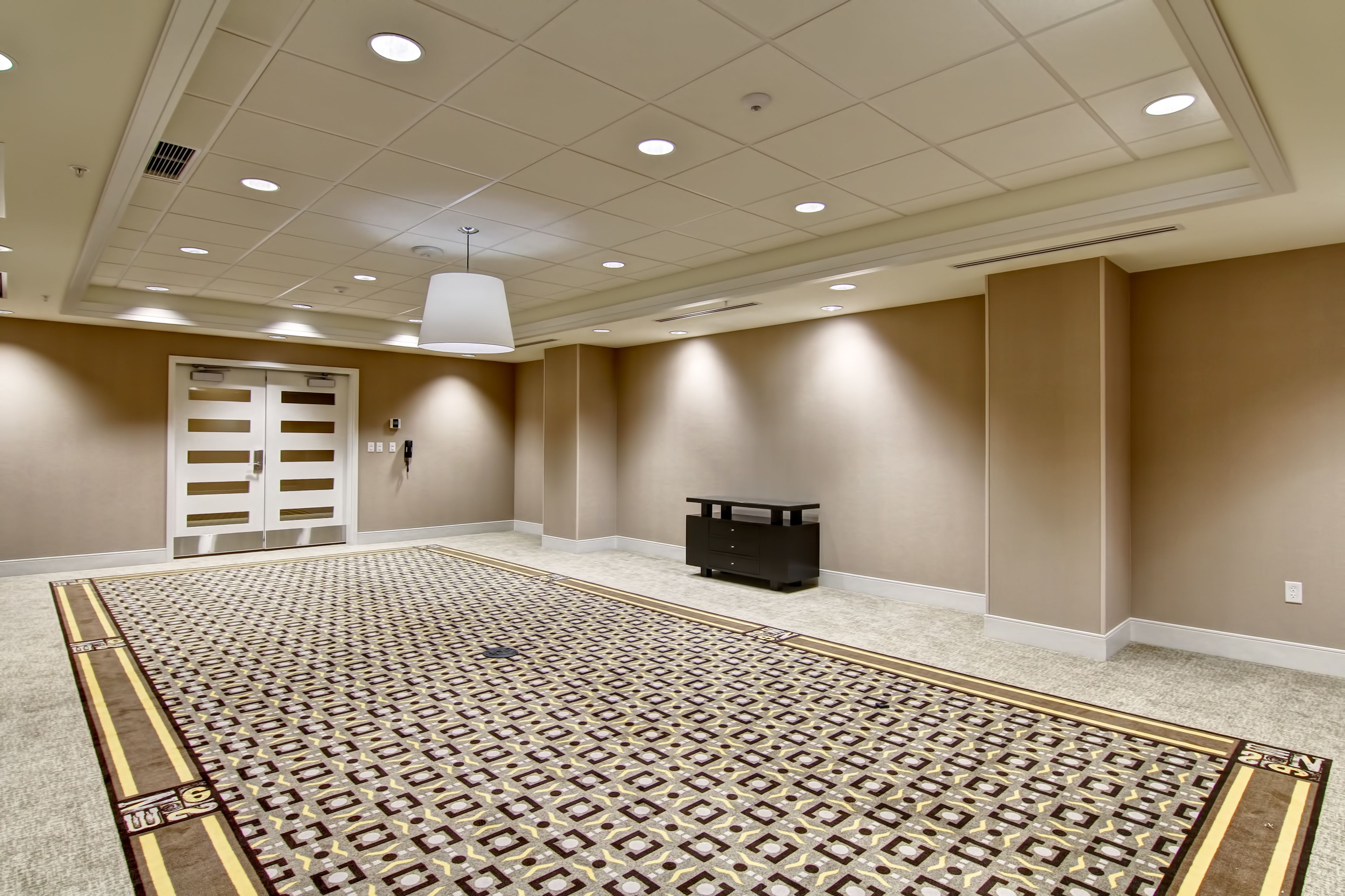 Una habitación amplia con alfombra estampada, paredes color beige e iluminación empotrada en el techo.