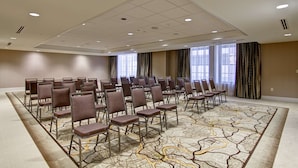 Une salle de conférence avec des rangées de chaises, de grandes fenêtres et un tapis à motifs.