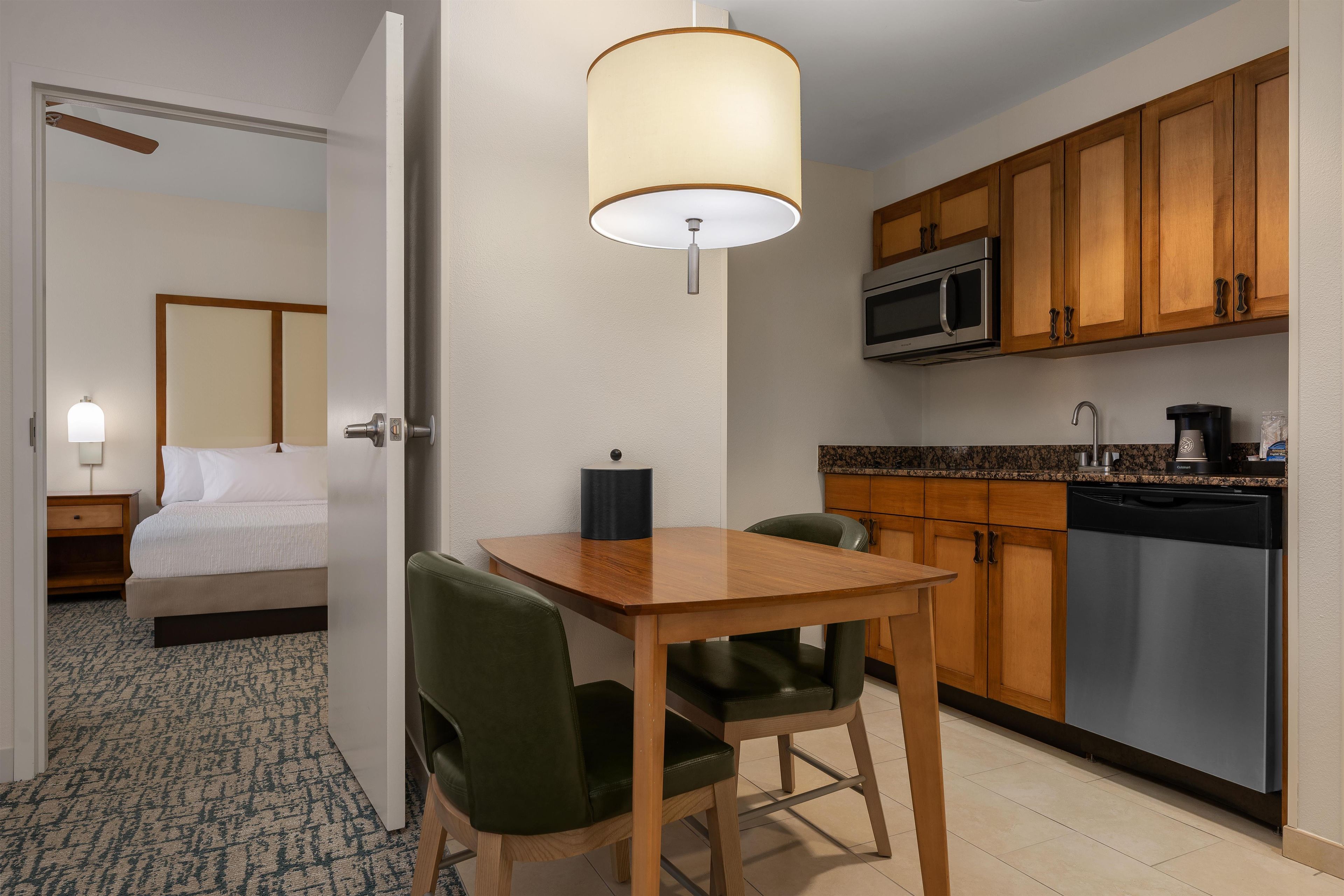 A hotel room with a bed, a desk with a chair, a kitchenette with a microwave, and a sink.