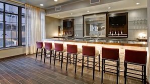 Un espace bar doté d’un long comptoir, de nombreux tabourets de bar rouges et d’une grande fenêtre agrémentée de rideaux.