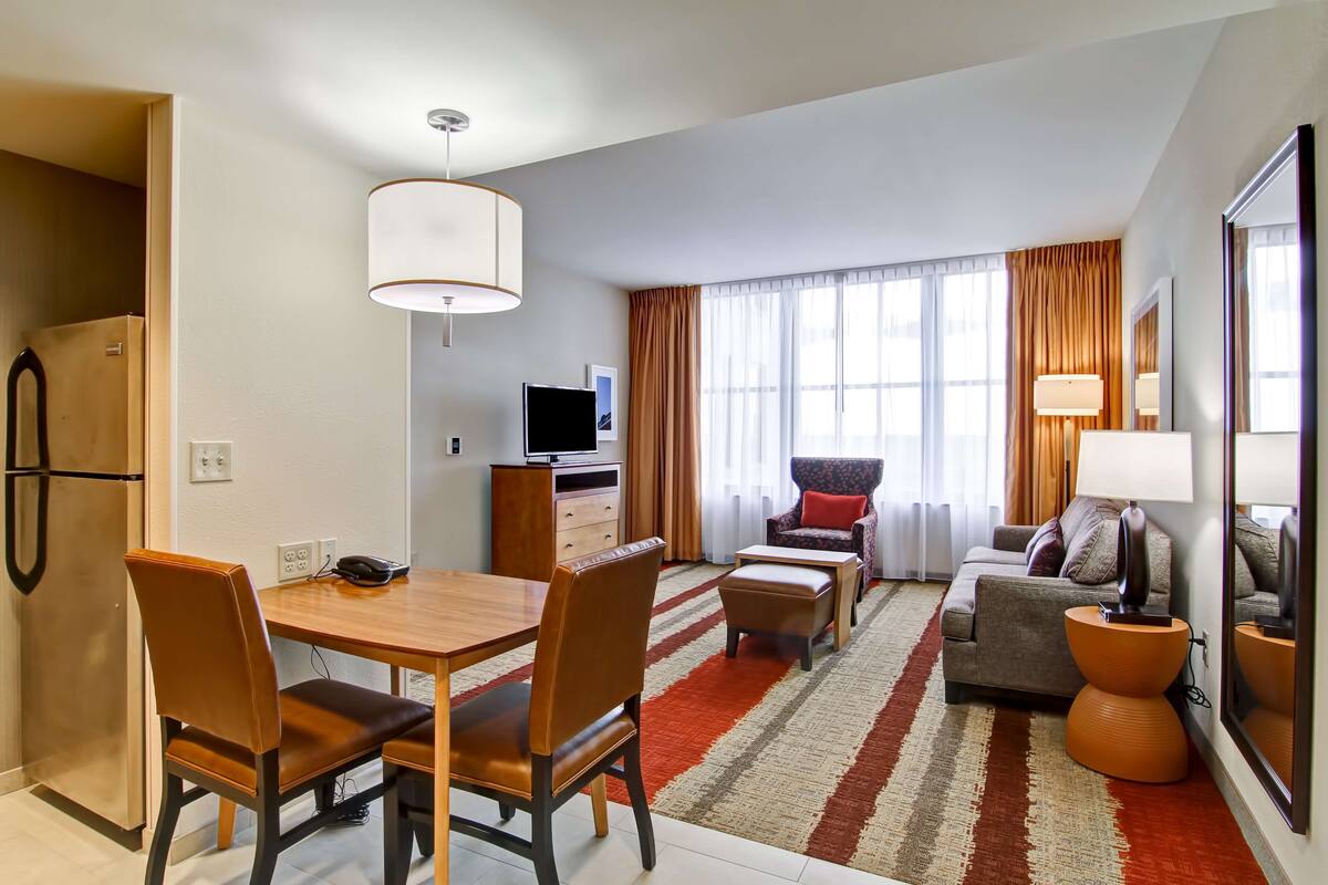 Een moderne hotelkamer met een zithoek, een bank, een televisie en een groot raam met gordijnen.