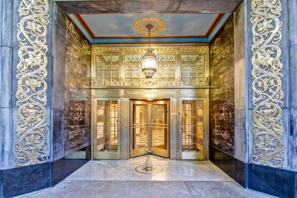 Una entrada imponente con detalles en oro ornamentados, un candelabro y un letrero que dice 'ENQUIRER'.