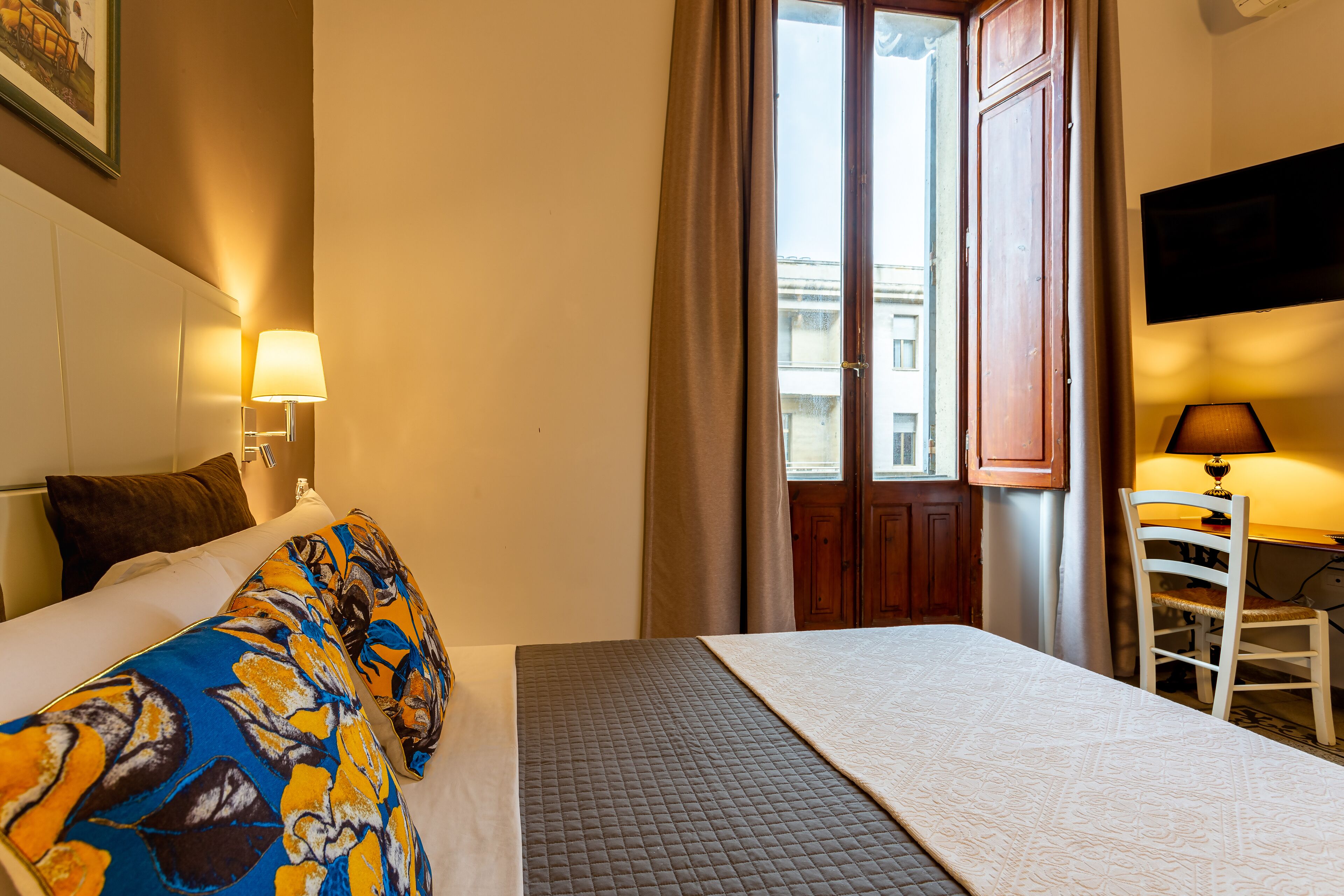 Ein Hotelzimmer mit Bett, Schreibtisch, Stuhl, Fernseher und einem Fenster mit Vorhängen.
