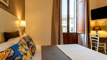 Ein Hotelzimmer mit Bett, Schreibtisch, Stuhl, Fernseher und einem Fenster mit Vorhängen.