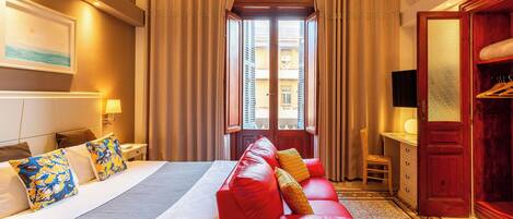 A hotel room with a large bed, a red sofa, a desk with a chair, and a wardrobe.