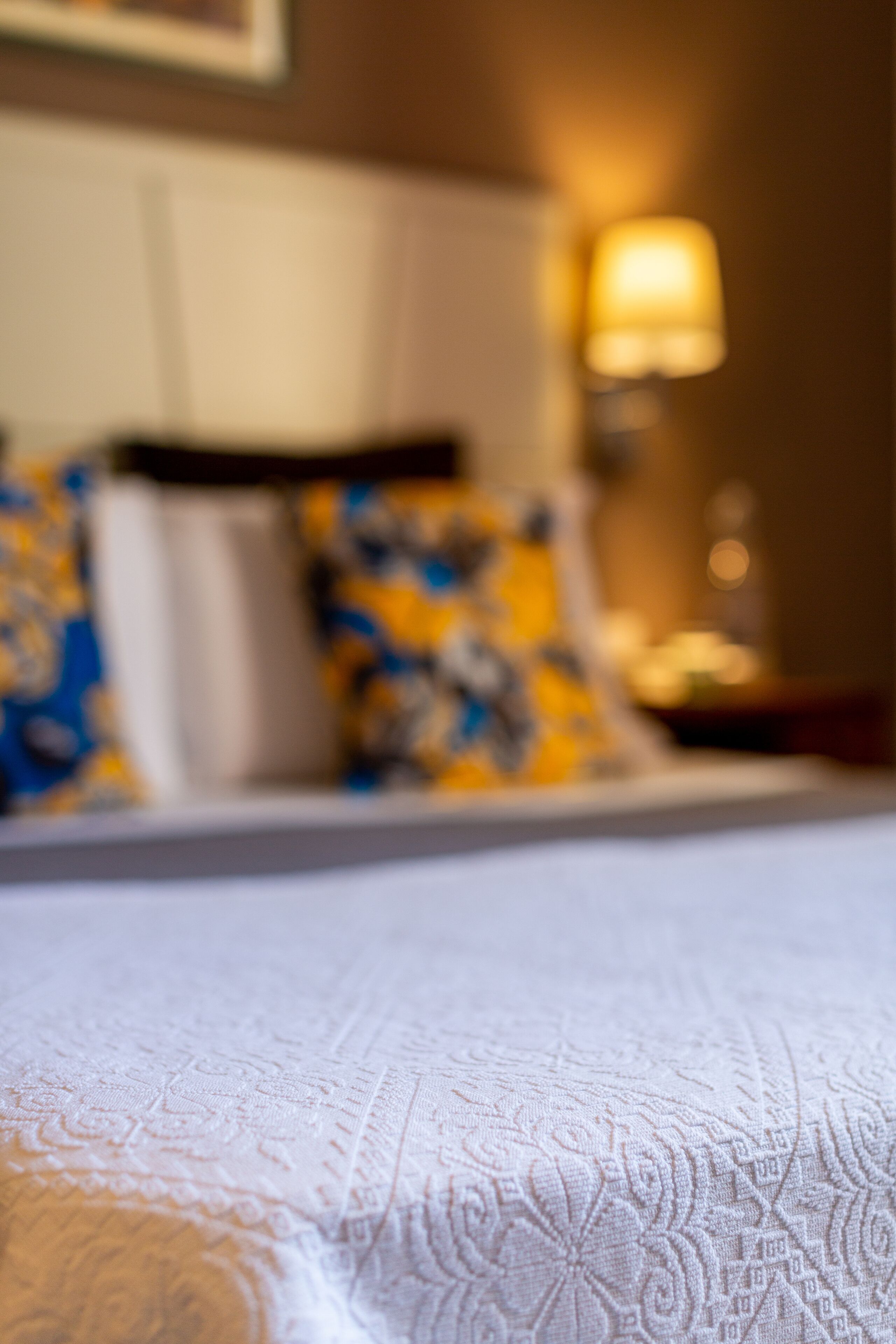Ein Bett mit einer weißen, kunstvoll gemusterten Bettdecke.
