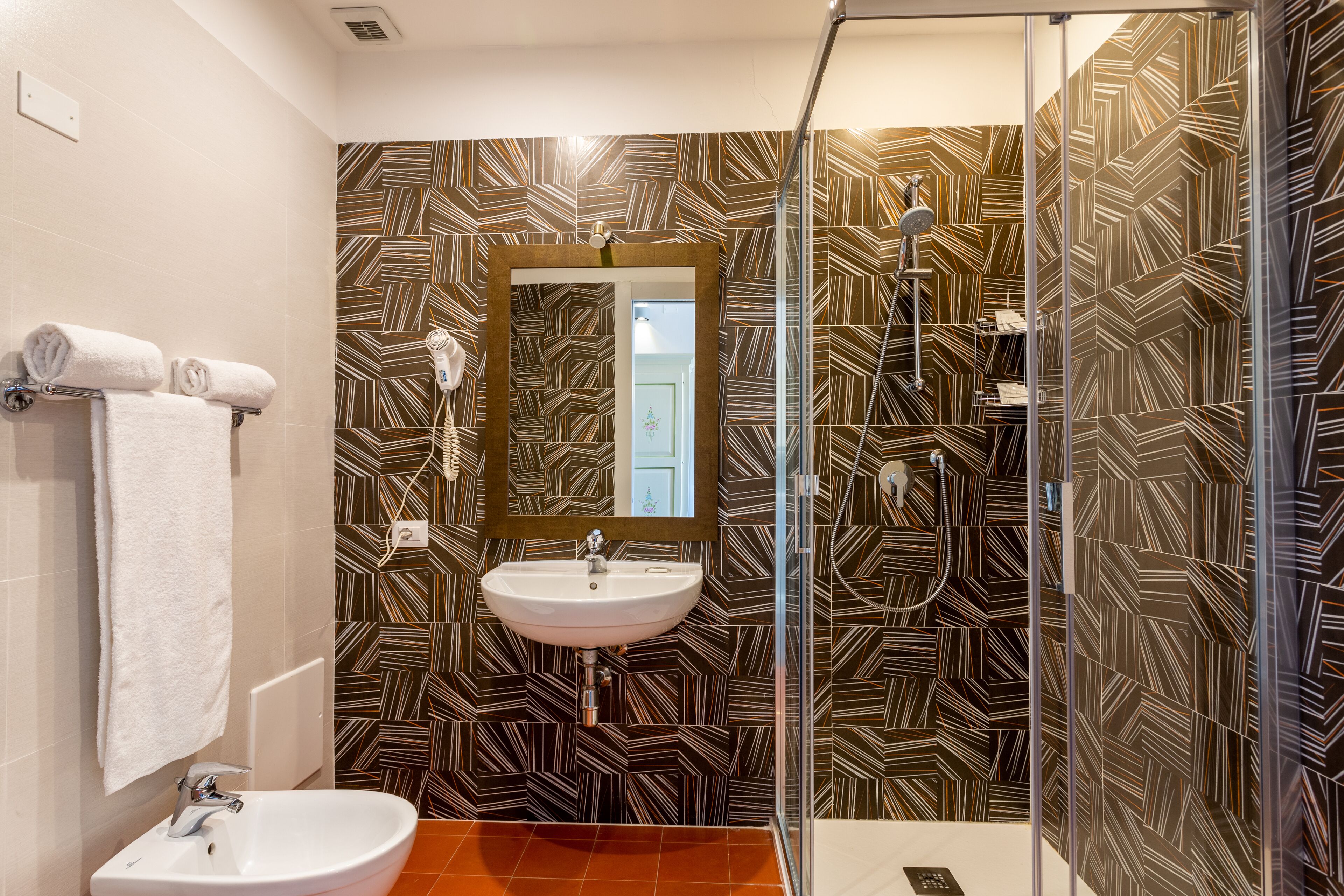 A modern bathroom with a geometric patterned wall, a white sink, and a glass shower enclosure.
