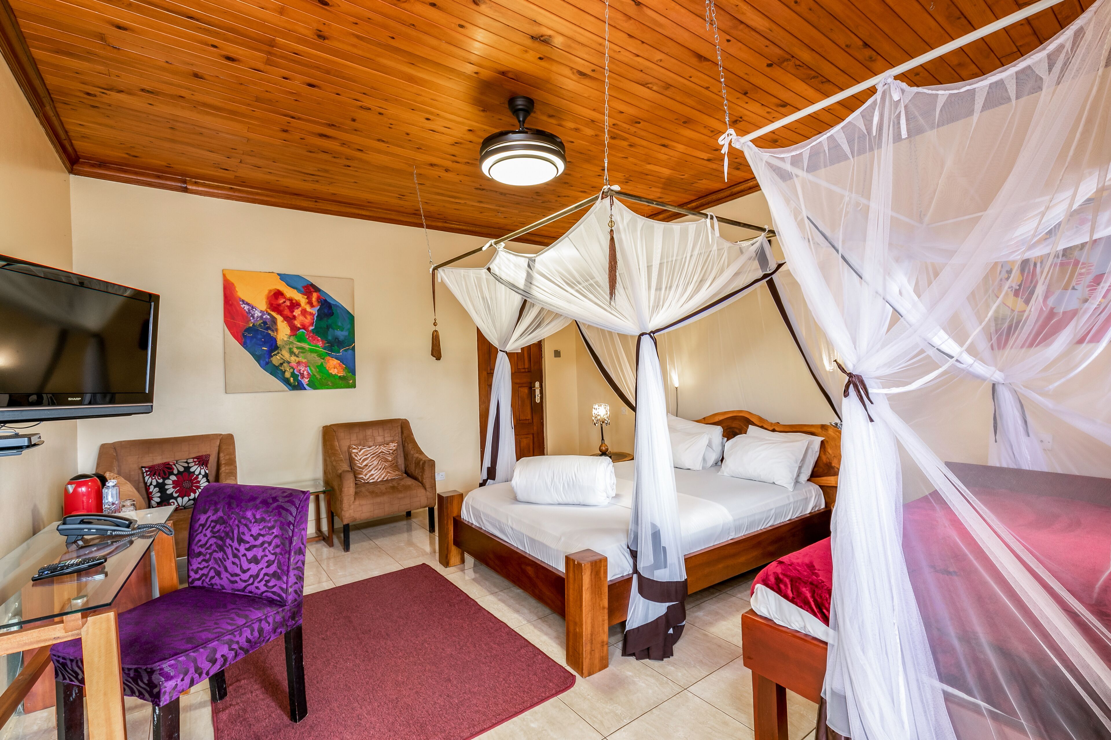 A bedroom with a bed, a chair, a desk, a TV, and a ceiling fan.