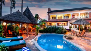 A pool area with lounge chairs and a thatched-roof structure. - 2 Friends Beach Hotel (Entebbe)