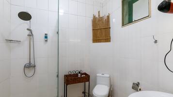 A bathroom with a glass-enclosed shower, a toilet, a sink, and a bamboo shelf.