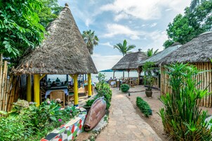 A tropical resort with thatched-roof huts, a stone pathway, and lush greenery.