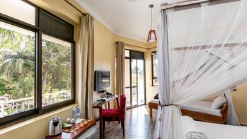 Una habitación con cama, escritorio, silla, televisión y ventanas grandes con cortinas.
